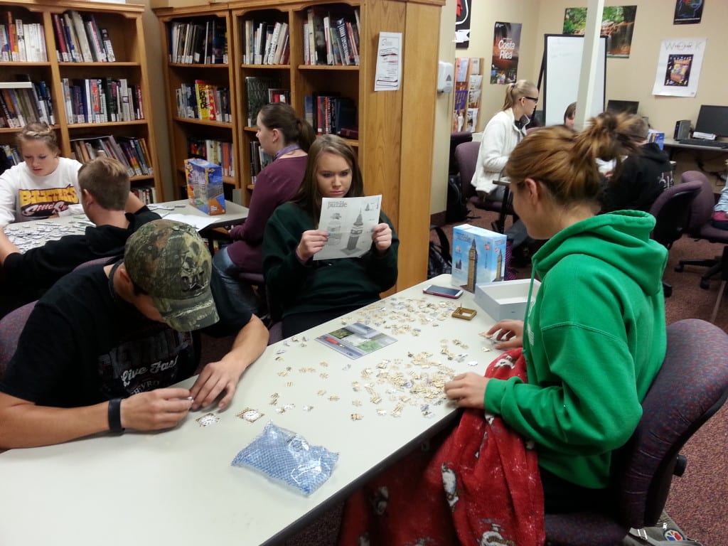 students sitting around tables in a library working on putting puzzles together