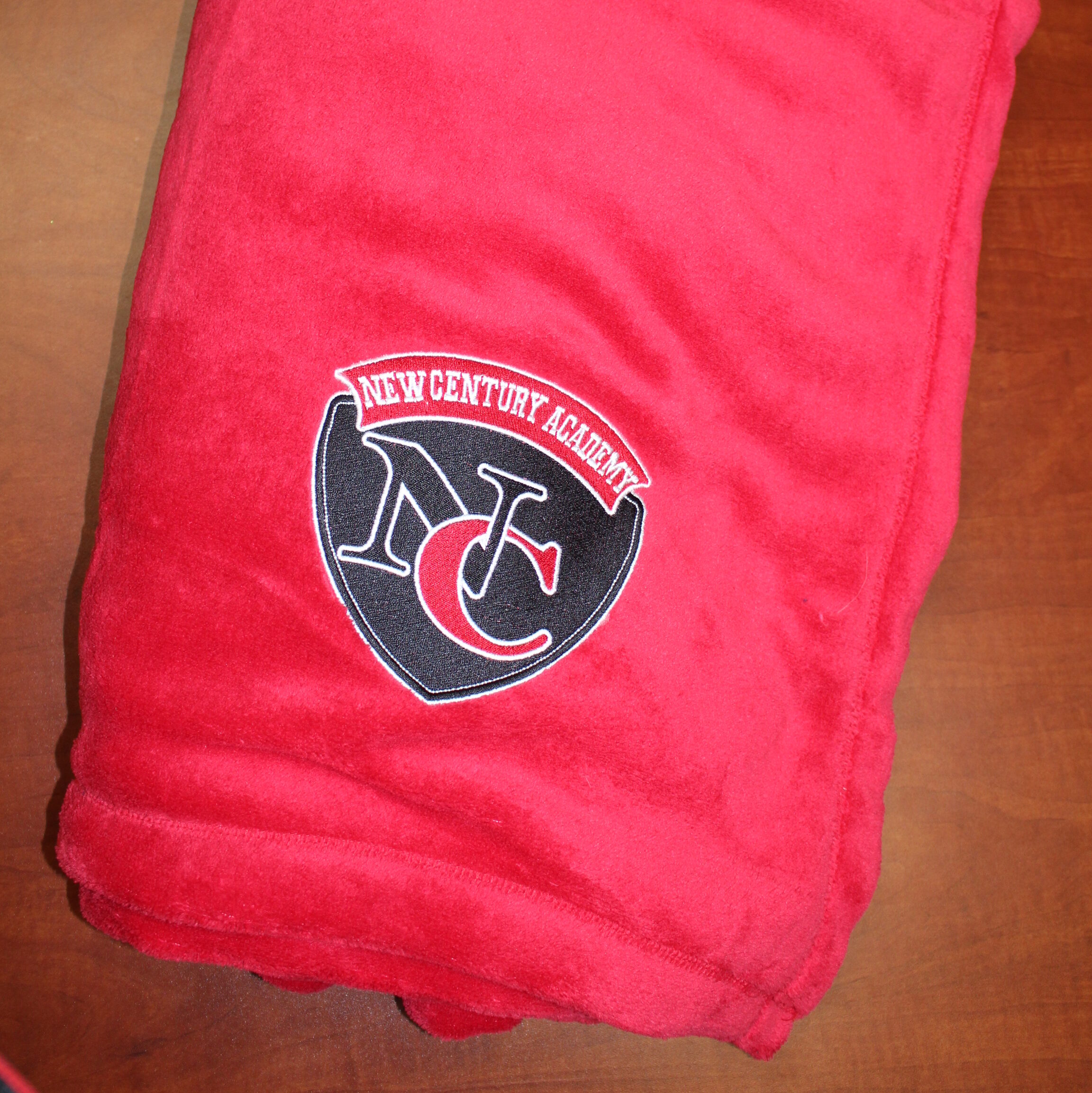 Red fleece blanket with the New Century Academy logo on it