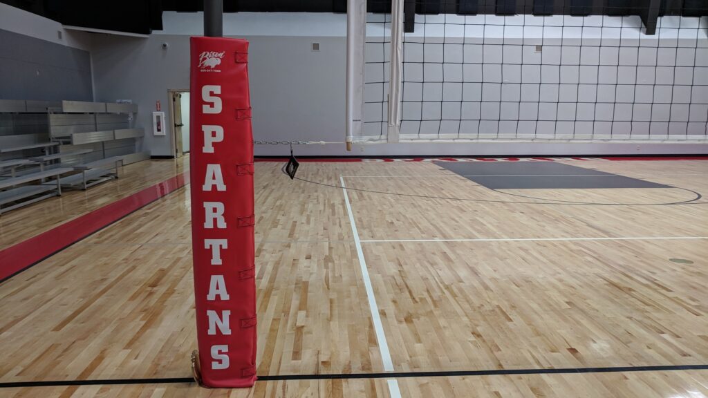 volleyball net set up in gymnasium with a safety pad spelling out the school's mascot, "Spartans"